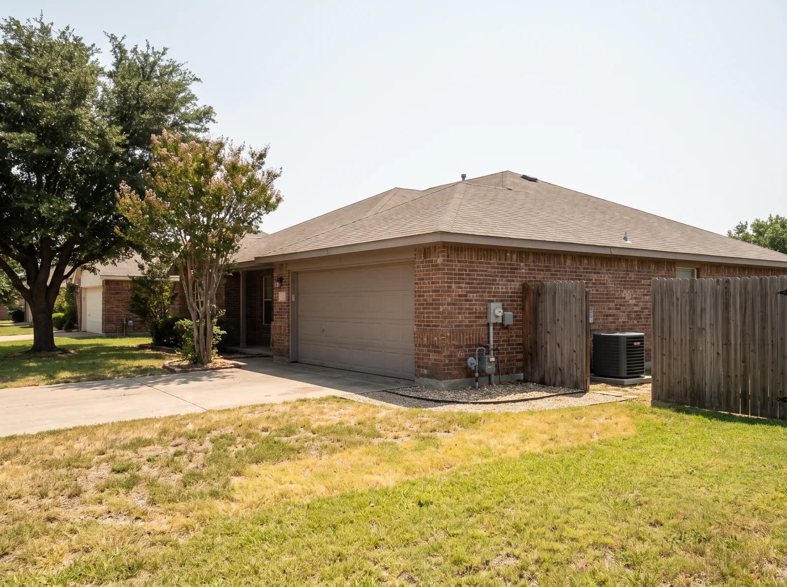 A single-story brick home in east Dallas on a hot summer afternoon, condenser at the side