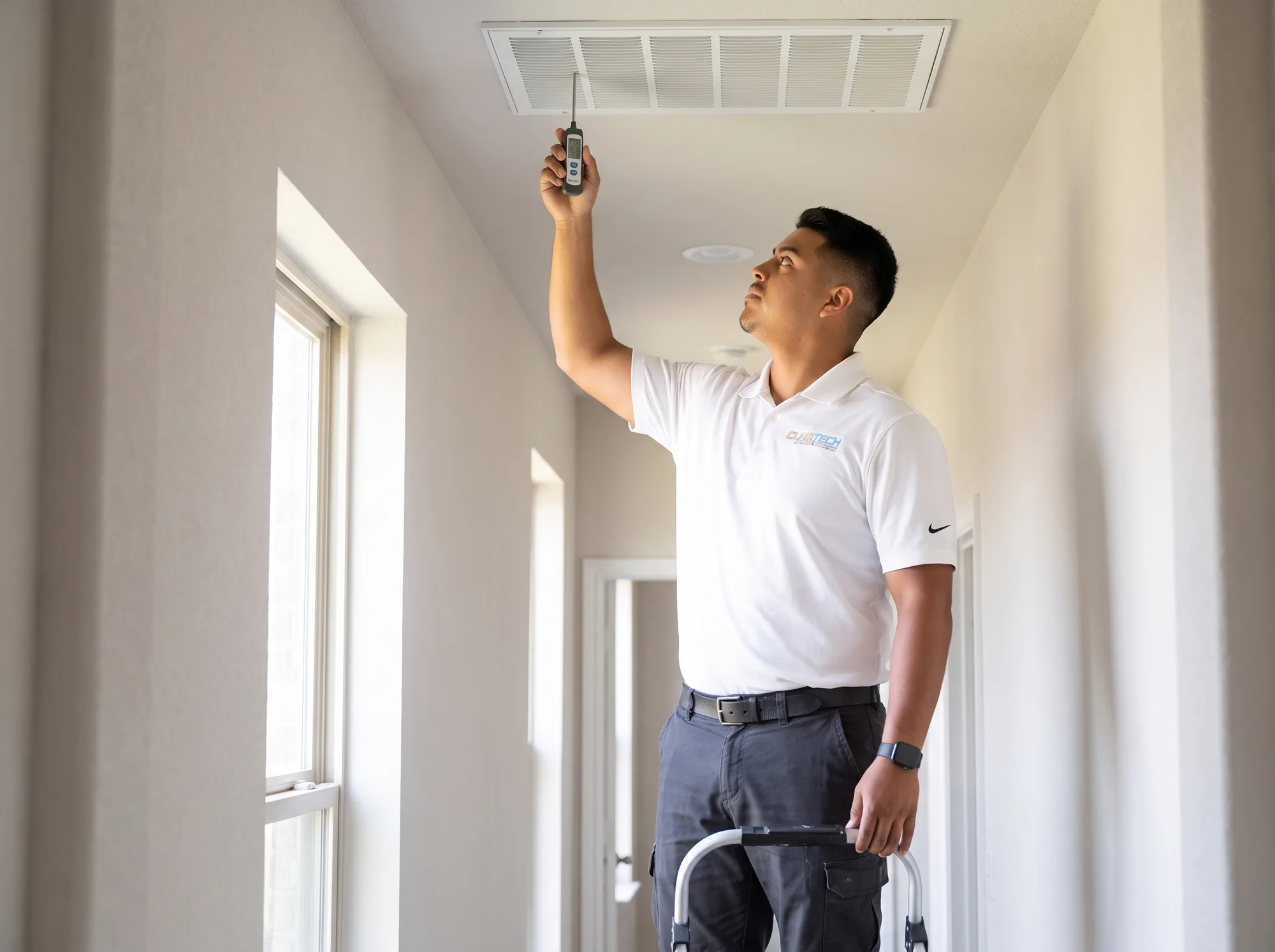 A technician holding a digital thermometer probe in a ceiling supply register to read heat pump supply air temperature