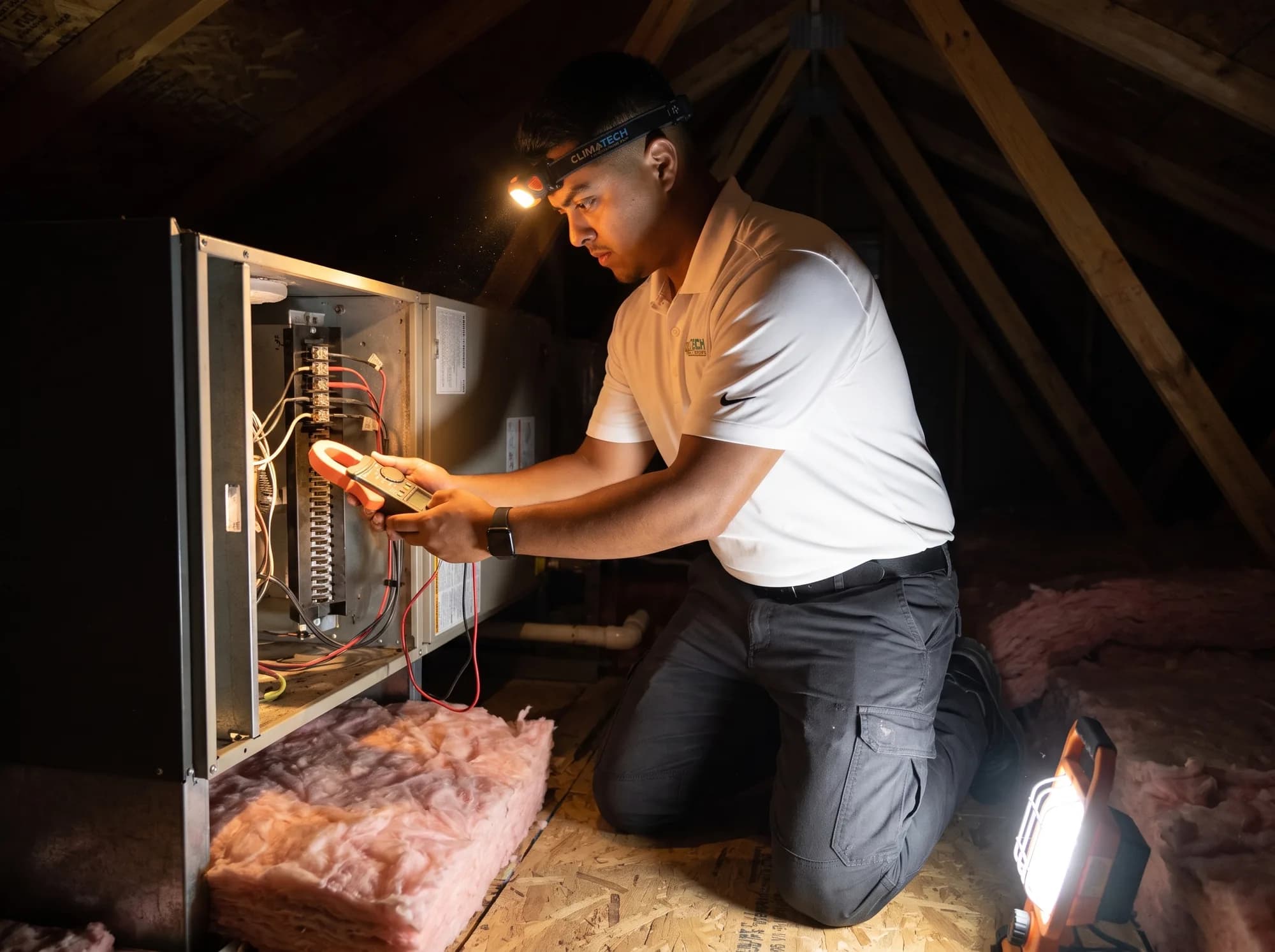 A technician testing the electric heat strip terminals inside an opened air handler with a clamp meter